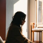 Erschöpfte Mama sitzt müde am Fenster im warmen Morgenlicht