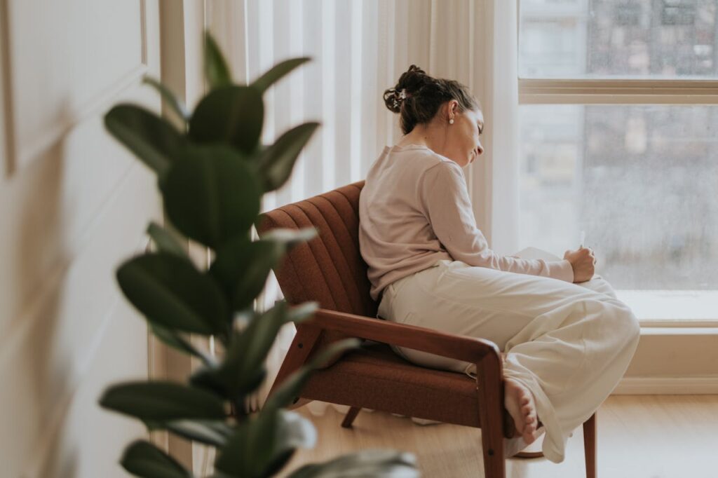 Mutter sitzt ruhig im Sessel und schreibt, um Gedanken zu ordnen und ihr Nervensystem zu beruhigen