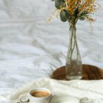 Tasse Kaffee auf einem Bett mit Blumen im Hintergrund – ruhiger Moment im Mama-Alltag zur Beruhigung des Nervensystems
