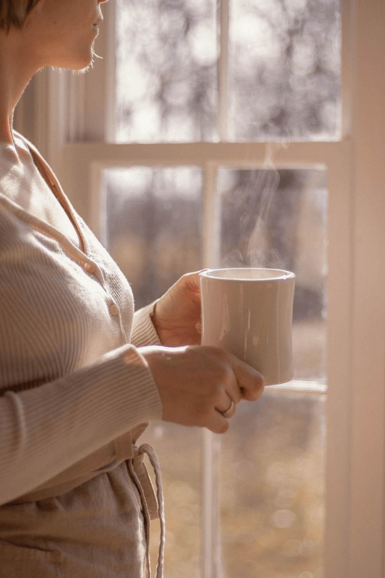 Frau mit Tasse am Fenster am Morgen - Müdigkeit und sanfte Morgenroutine für mehr Energie im Mama-Alltag