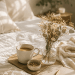 Gemütliche Szene mit einer Tasse Kaffee, Notizbuch, Trockenblumen und einer weichen Decke auf einem Bett in warmem Morgenlicht – Sinnbild für Ruhe und ein reguliertes Nervensystem im Mama-Alltag.